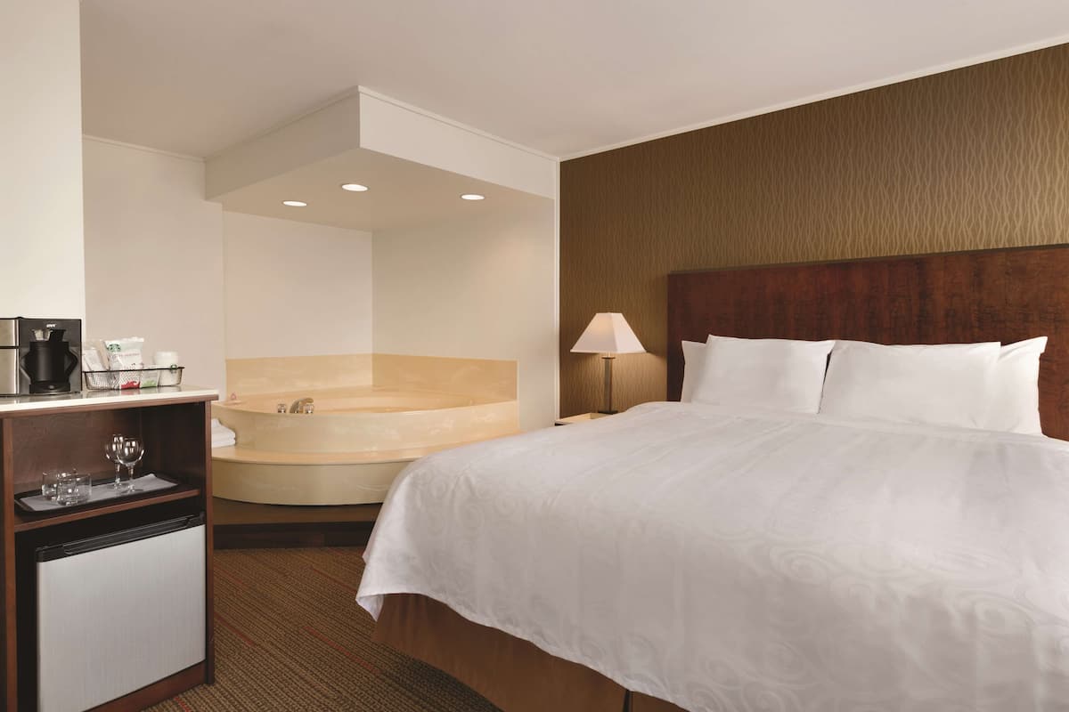 Habitación de hotel con cama, escritorio con cafetera, refrigerador y bañera.