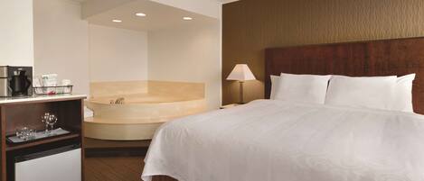 A hotel room with a bed, a desk with a coffee maker, a mini-fridge, and a bathtub.