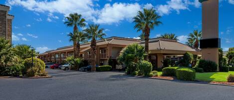 A hotel with a sign reading "Quality Inn by Choice Hotels," featuring a parking lot, palm trees, and a clear blue sky.