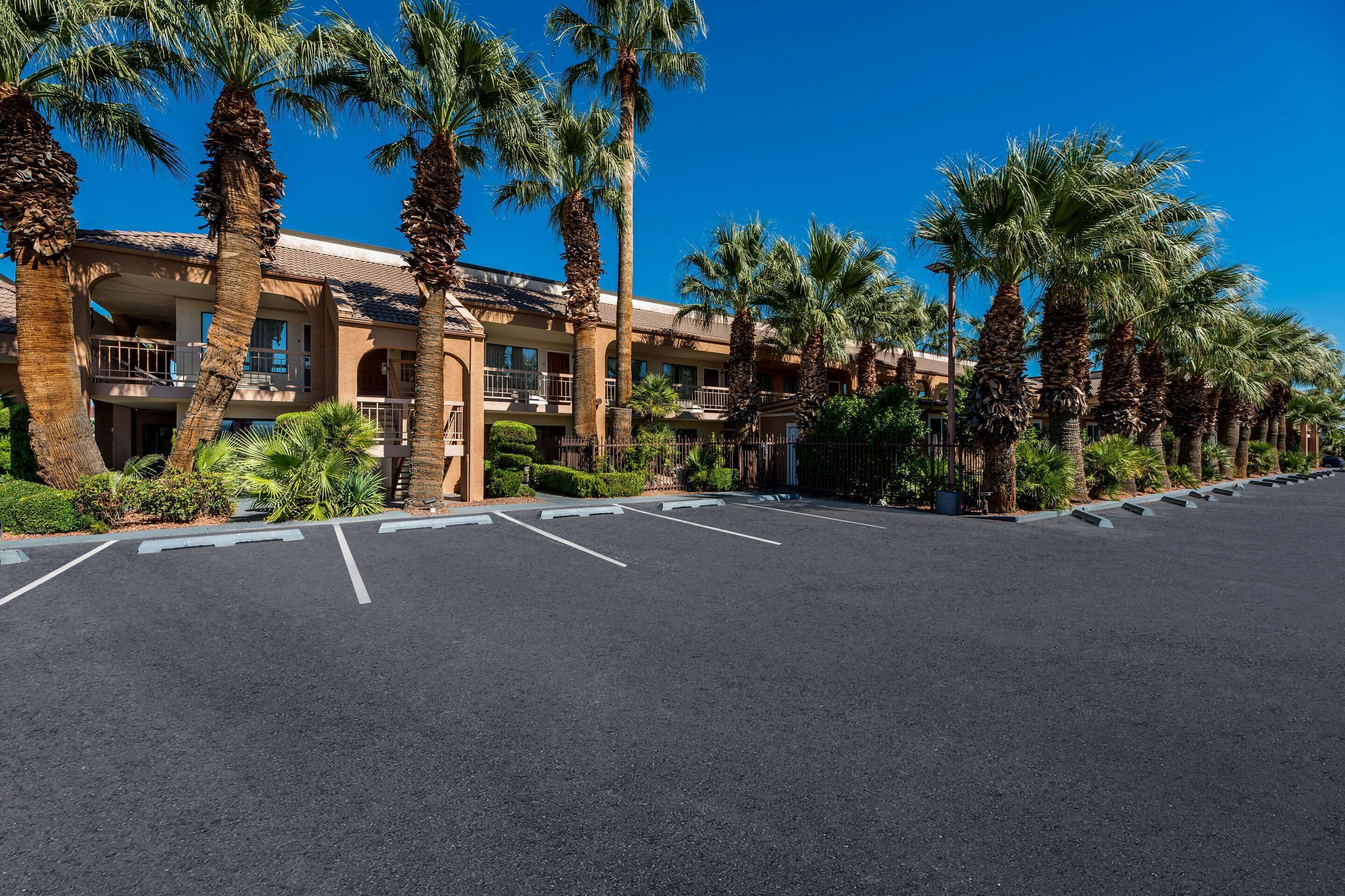 Un hotel con estacionamiento, palmeras y un cielo azul despejado.