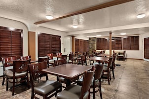 A spacious dining area with multiple wooden tables and chairs, a stone accent wall, and a white door.
