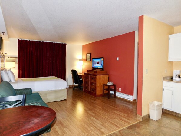 A hotel room with a bed, a desk with a television, a chair, and a small table.