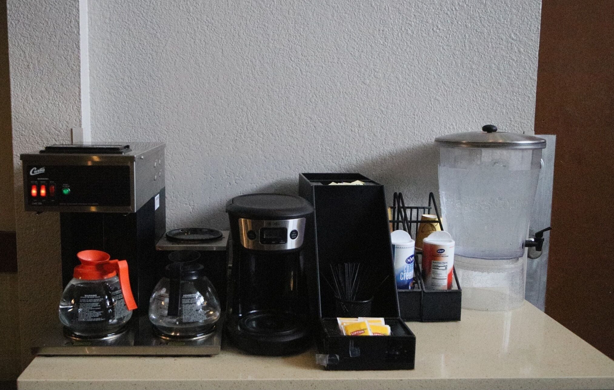 A coffee station with a coffee maker, a water dispenser, and various coffee pods.