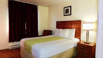 A hotel room with a bed, a nightstand, a lamp, a picture on the wall, and a window with curtains.