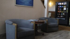 A seating area with two armchairs and a small round table, a vending machine, and a framed picture on the wall.