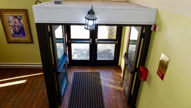 A room with a wooden floor, a white ceiling, a black bench, a window, a door, a wall-mounted light fixture, and a framed picture.