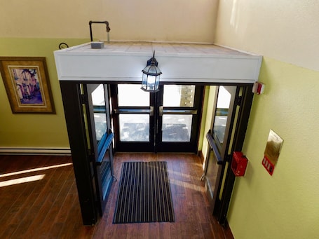 A room with a wooden floor, a white ceiling, a black bench, a window, a door, a wall-mounted light fixture, and a framed picture.