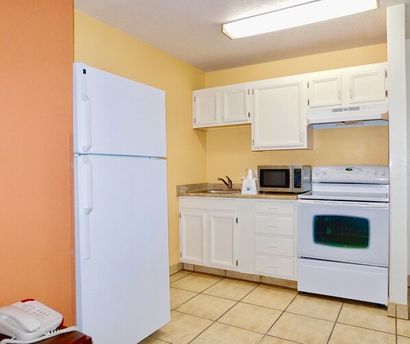 A compact kitchen with white appliances, including a refrigerator, microwave, and oven, against yellow walls. - Americas Best Value Inn & Suites Anchorage Airport (Anchorage)