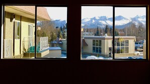 Two windows with a view of a building and snow-covered mountains.