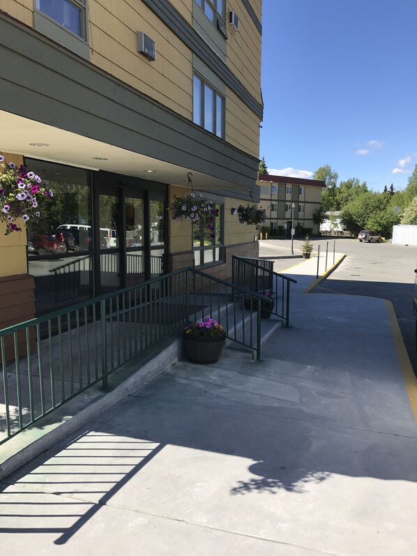 A building with a covered outdoor area, a parking lot, and hanging flower baskets. - Americas Best Value Inn & Suites Anchorage Airport (Anchorage)