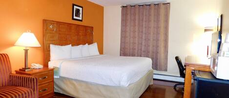 Une chambre d’hôtel avec un lit, une chaise, un bureau avec un ordinateur et une lampe.