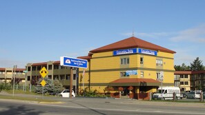 A yellow building with "Executive Suite Hotel" signs, a speed limit sign of 25 mph, and a directional sign for "Americas Best Value Inn & Suites." - Americas Best Value Inn & Suites Anchorage Airport (Anchorage)
