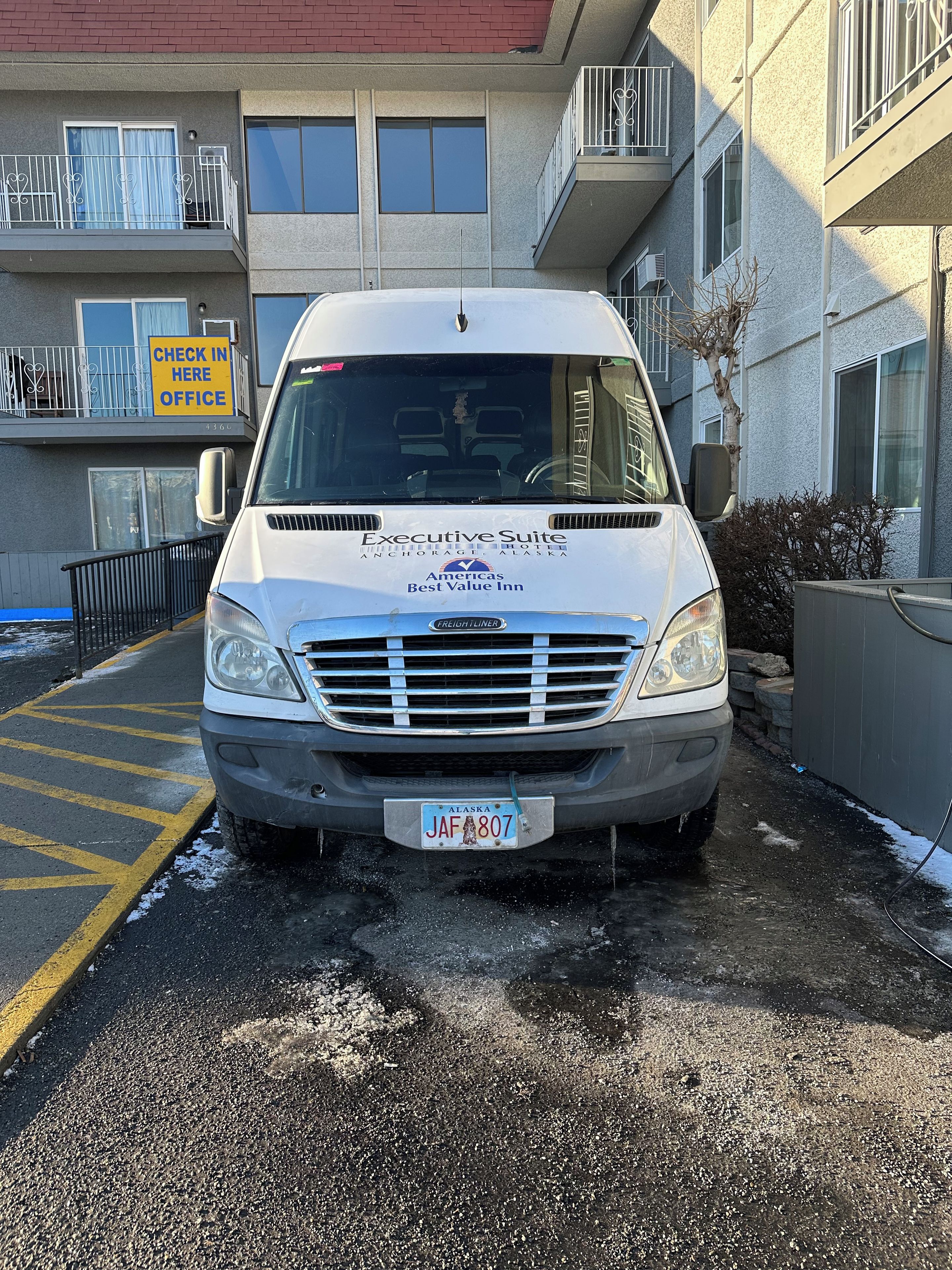 Una camioneta blanca estacionada frente a un edificio con un letrero que dice 'Check In Here Office'.