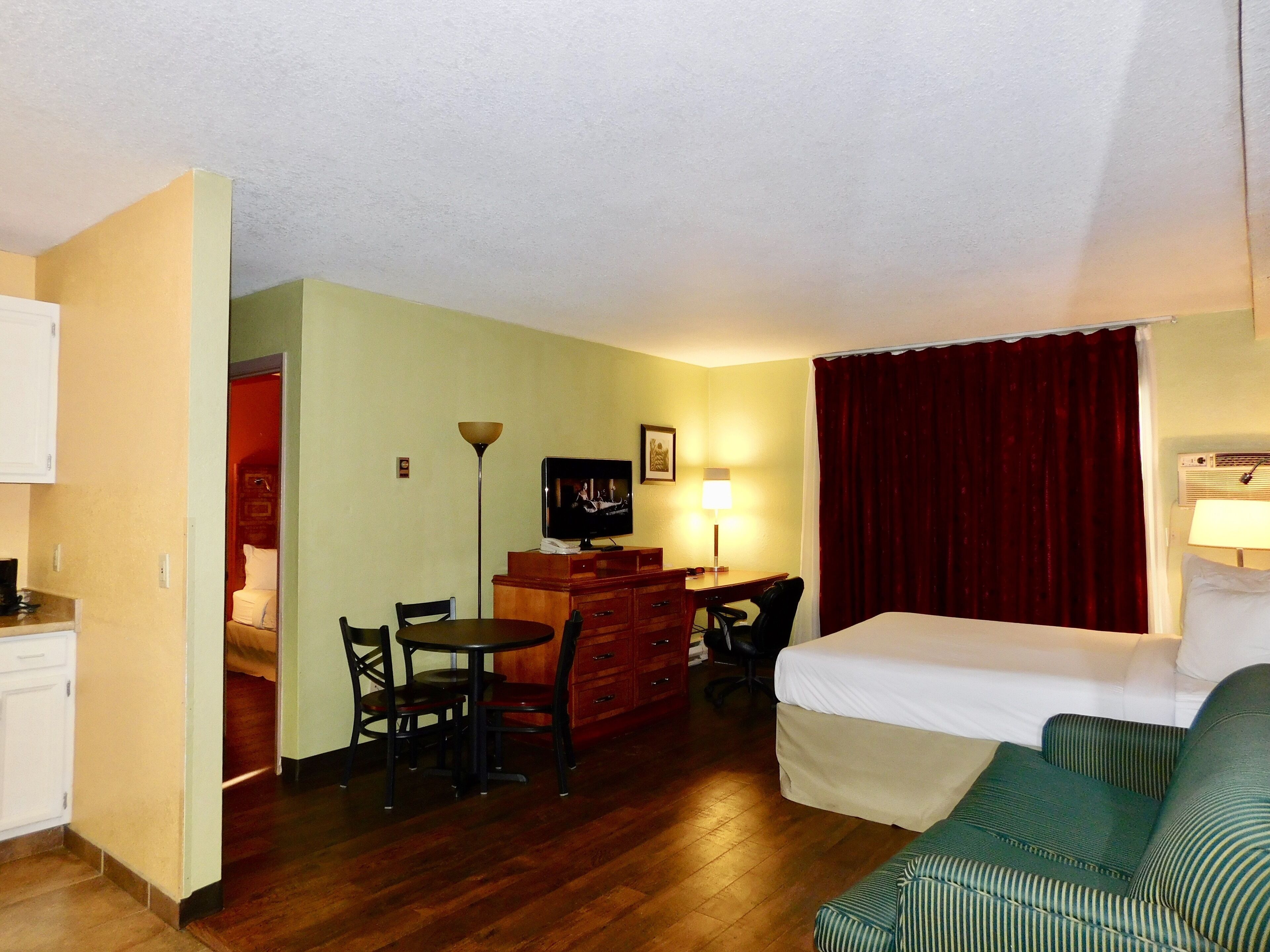 A hotel room with a bed, a green-striped sofa, a desk with a chair, a television, and a lamp.