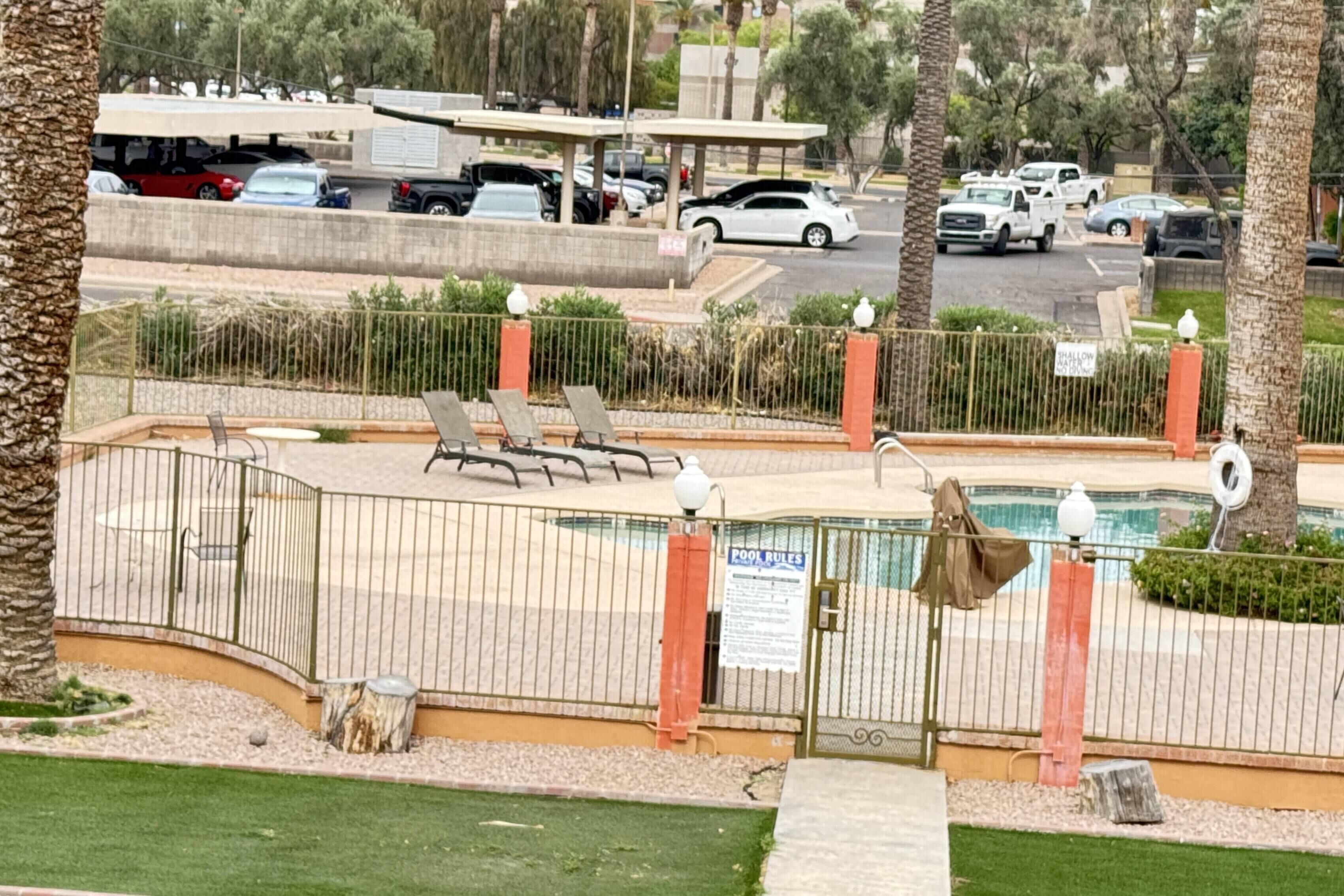 A pool area with a fence, lounge chairs, and a sign indicating pool rules.