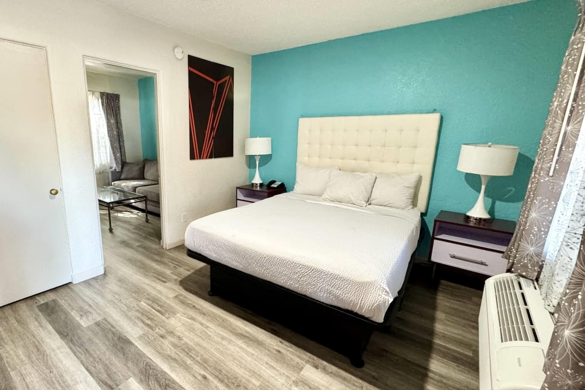 Une chambre à coucher comprenant un lit, deux tables de chevet, une commode, une chaise et une fenêtre avec des rideaux.