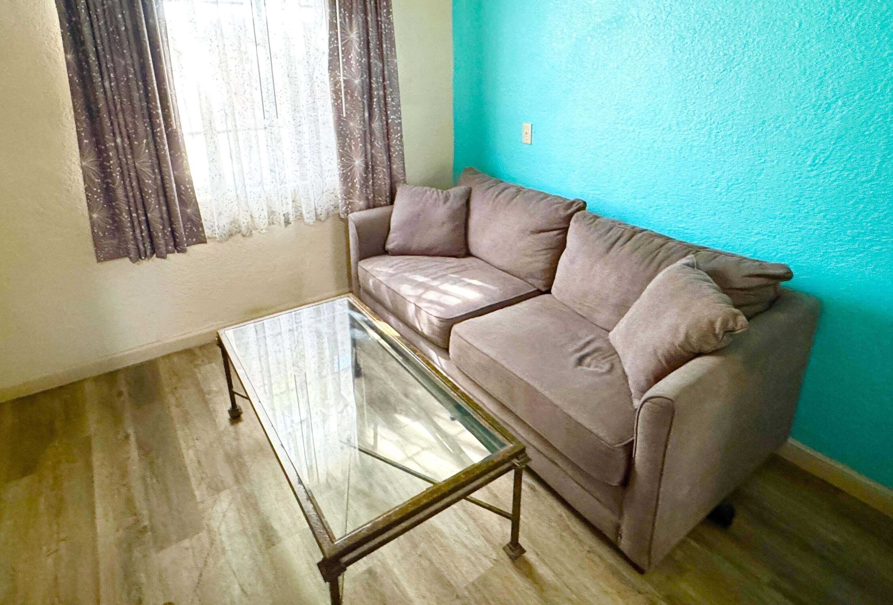 Una sala de estar con un sofá color beige, una mesa de centro de vidrio y una pared verde azulado.