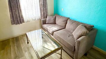 Una sala de estar con un sofá color beige, una mesa de centro de vidrio y una pared verde azulado.