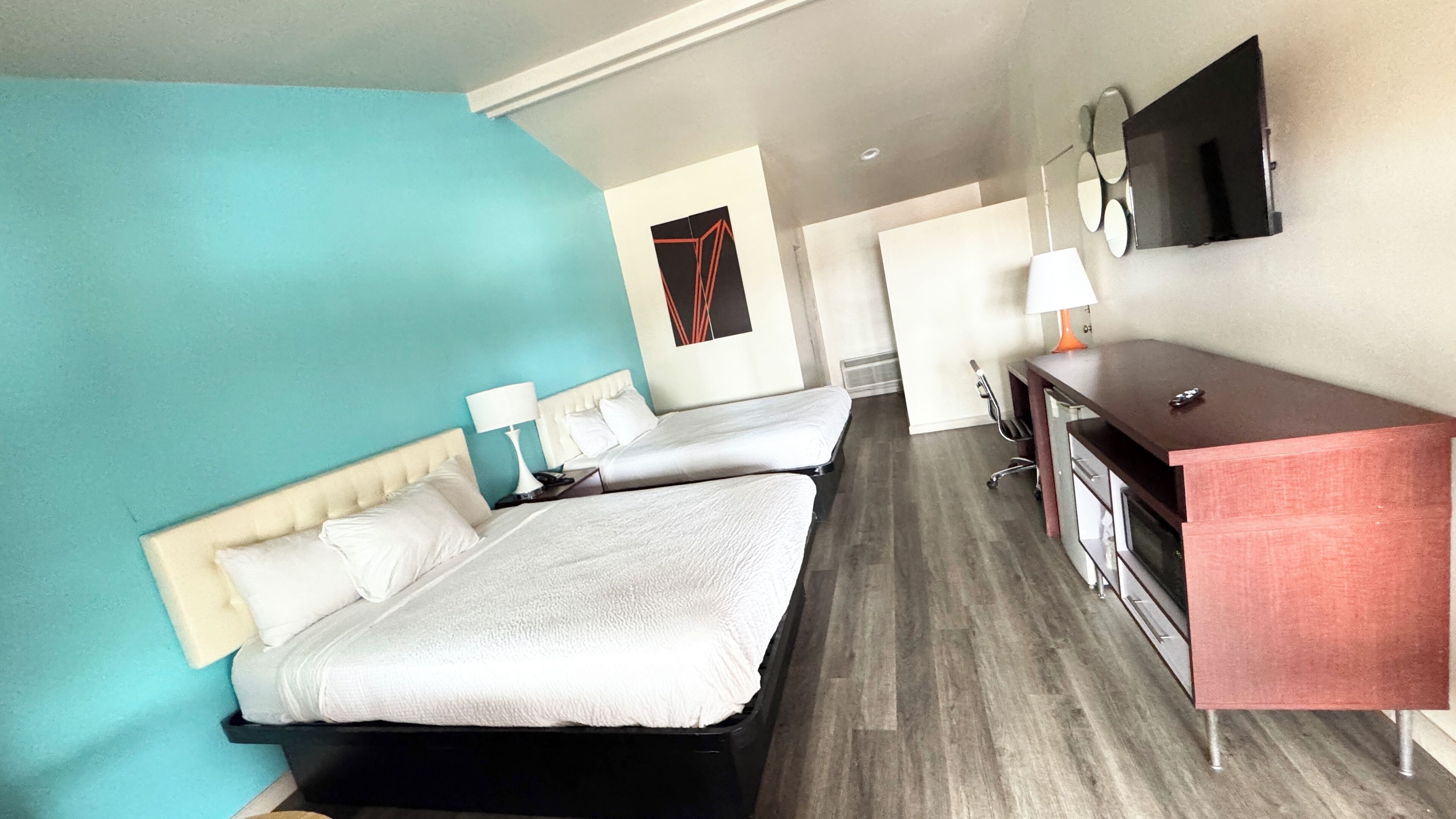 Une chambre d’hôtel avec deux lits, un bureau, une chaise, une télévision et un miroir.