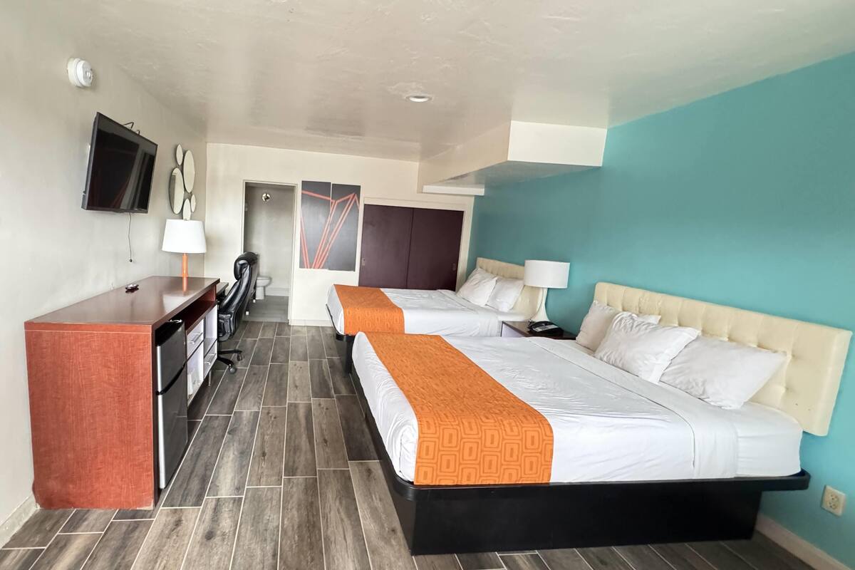 Une chambre d’hôtel avec deux lits, un bureau, une télévision et une porte donnant sur une autre chambre.