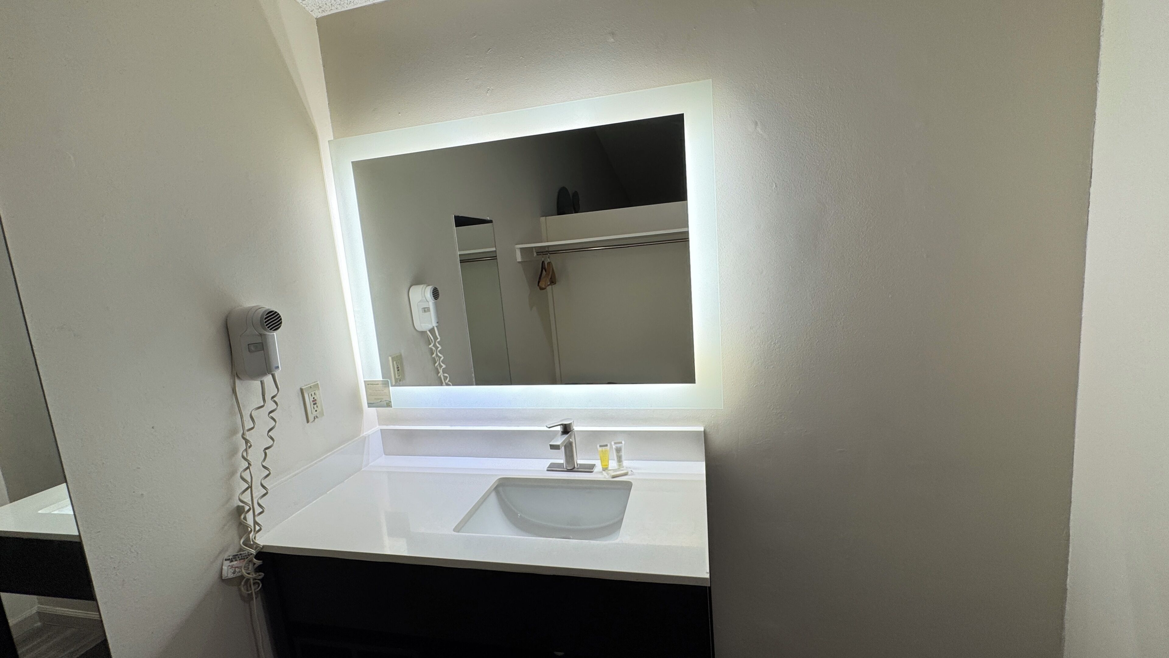 Un baño con un lavamanos blanco, un espejo y un secador de pelo montado en la pared.