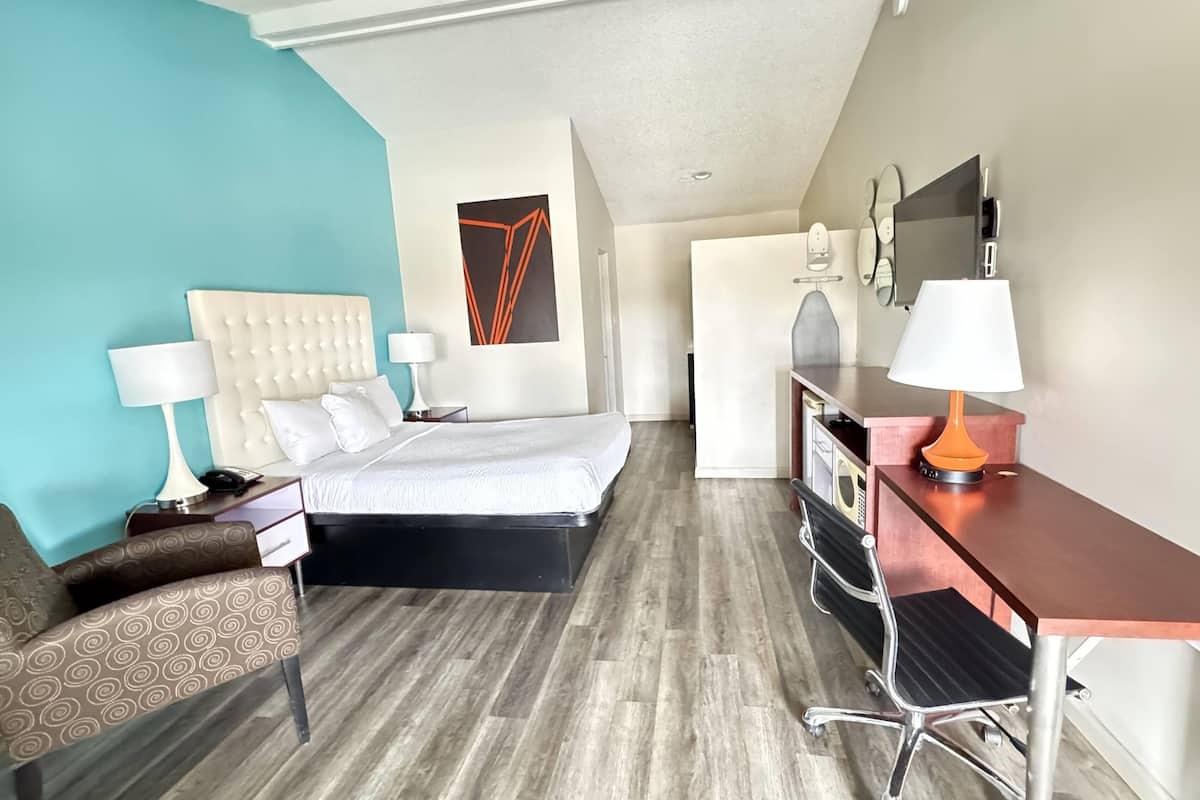 Une chambre d’hôtel équipée d’un lit, d’un bureau, d’une chaise, d’une lampe et d’un téléviseur fixé au mur.