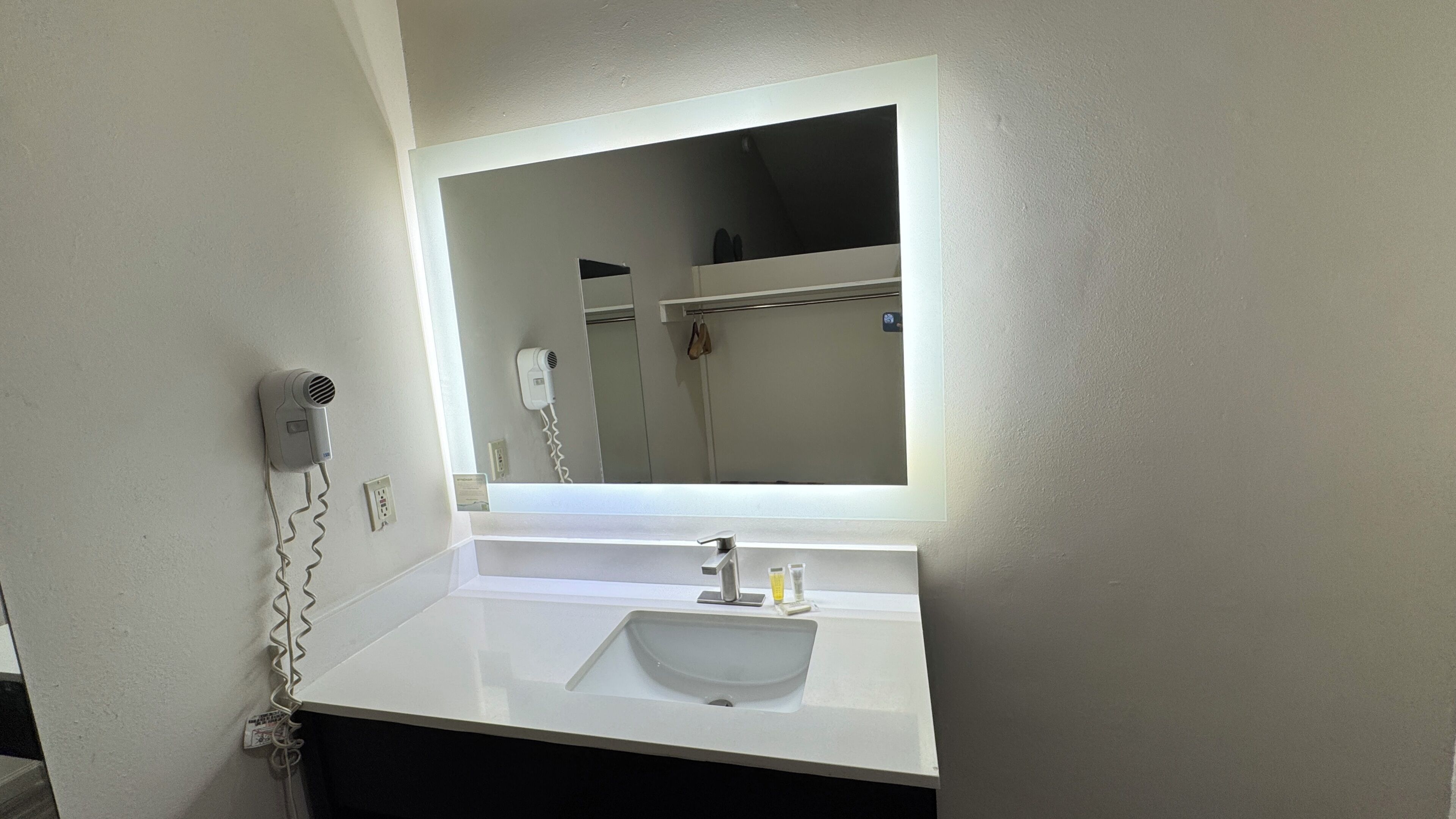 A bathroom with a white sink, a mirror, a hairdryer, and a towel rack.