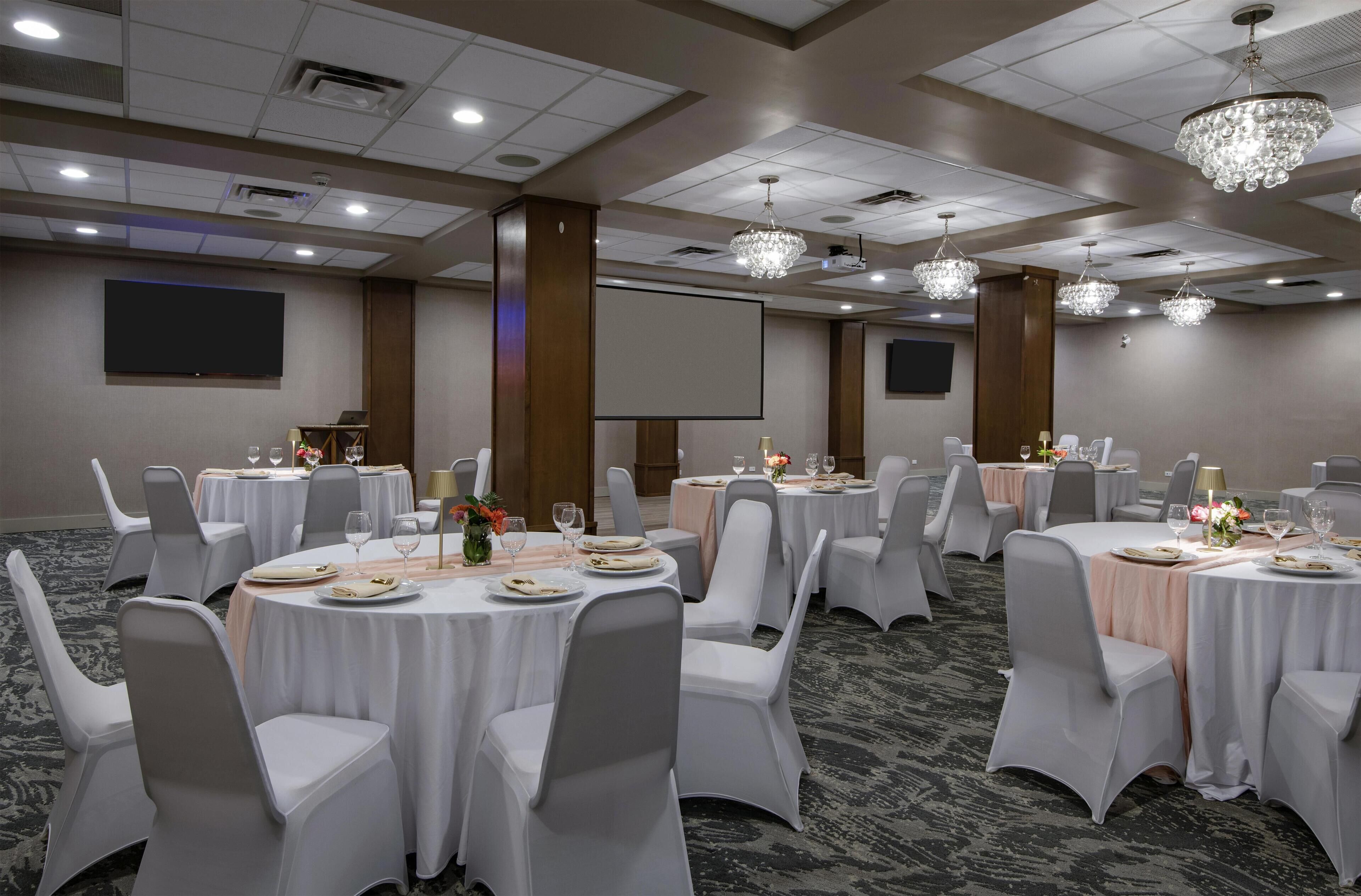 A conference room with round tables, white chairs, and chandeliers.