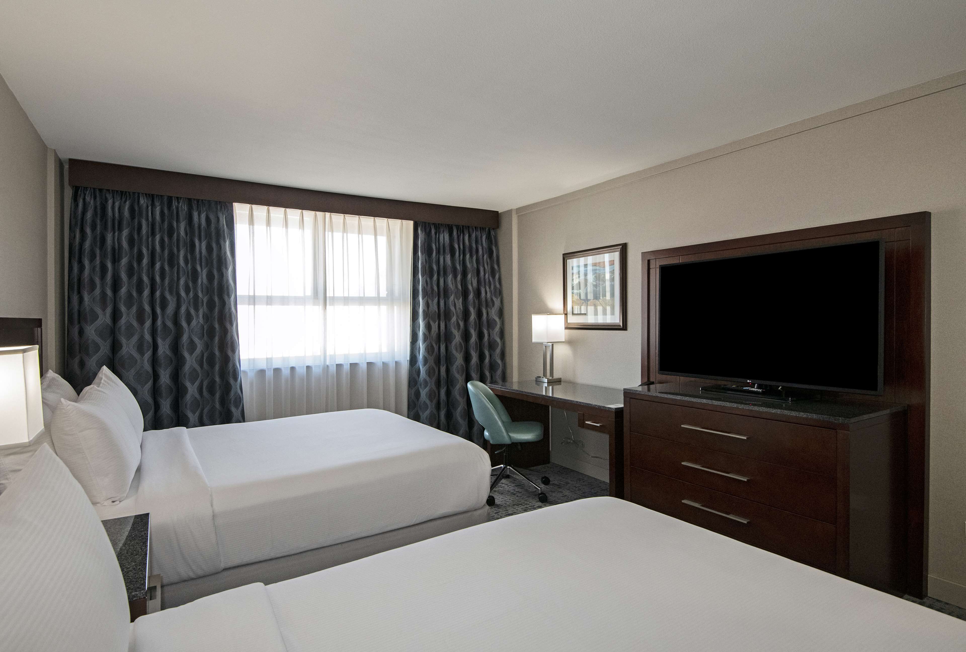 A hotel room with two beds, a desk with a chair, a television, and a window with curtains.