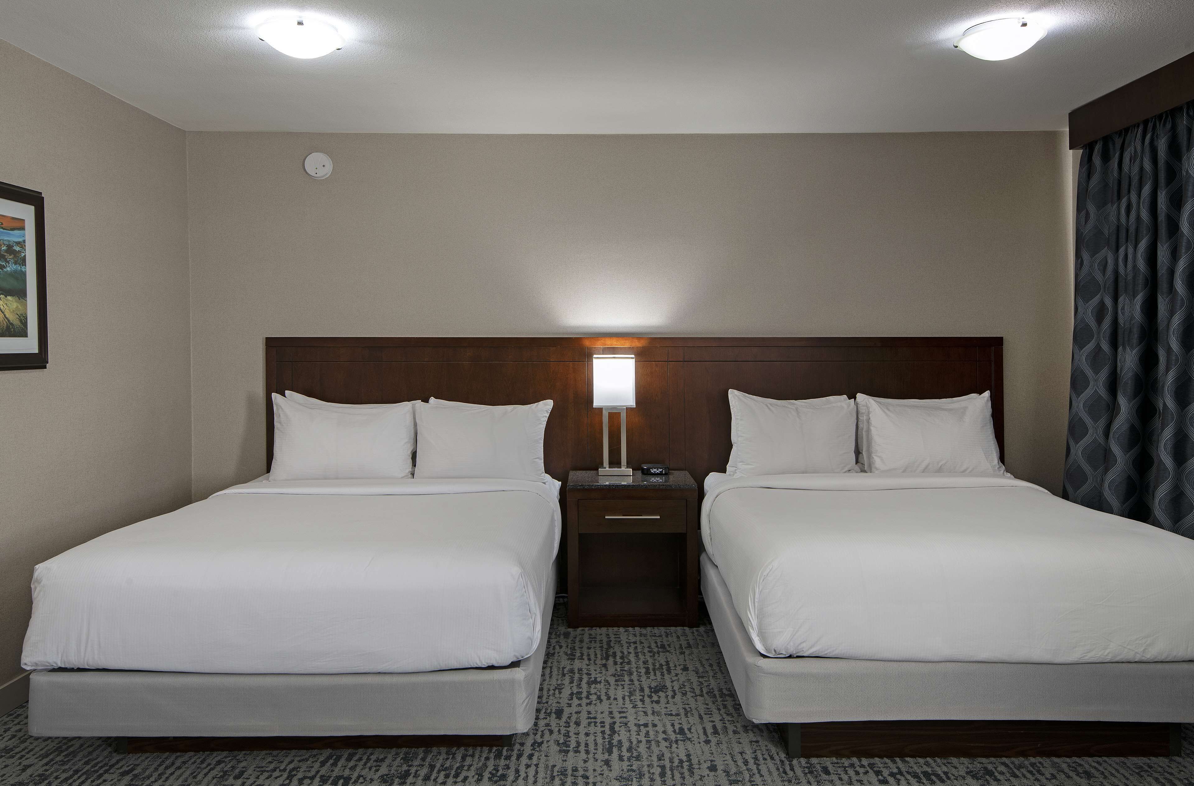 Une chambre d’hôtel avec deux lits simples, une table de chevet entre les deux et une lampe fixée au mur.