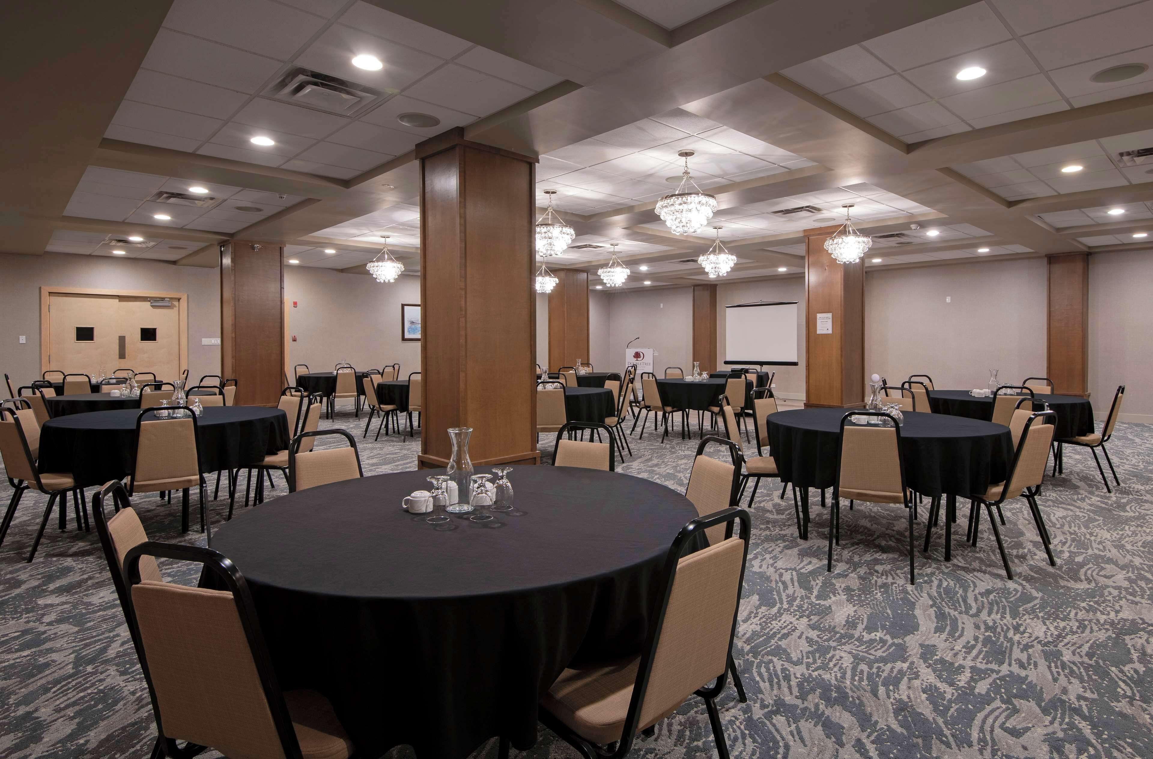 A conference room with multiple round tables, beige chairs, and chandeliers.