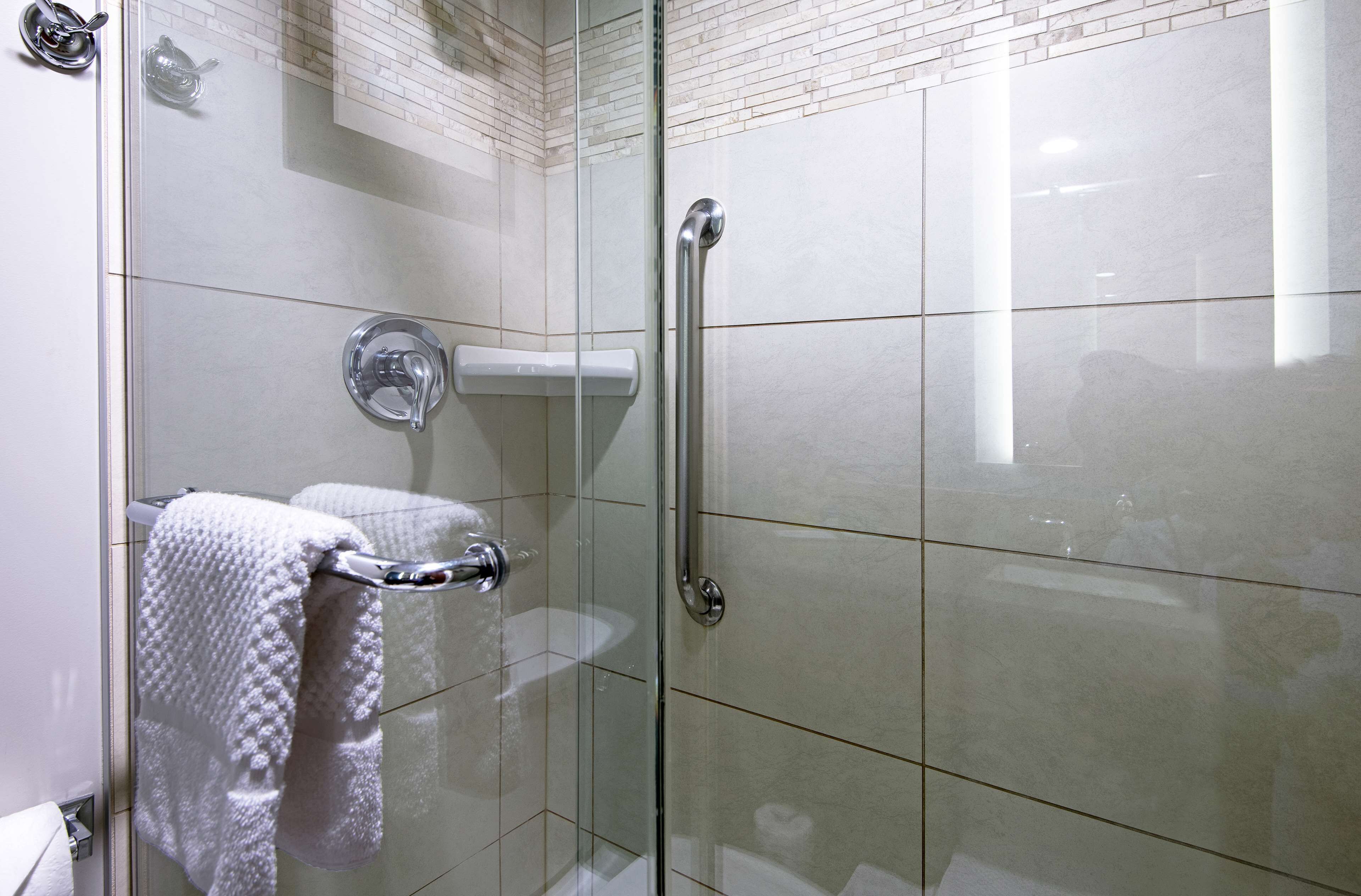 A glass-enclosed shower with a white towel hanging on a rack, a glass door, and a handrail.