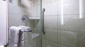 A glass-enclosed shower with a white towel hanging on a rack, a glass door, and a handrail.