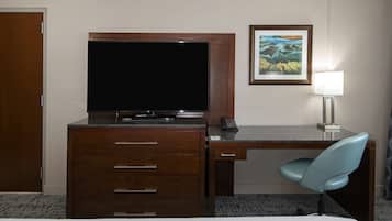 Habitació d'hotel amb escriptori de fusta, televisió de pantalla plana, làmpada de taula, quadre al mur i cadira blava.