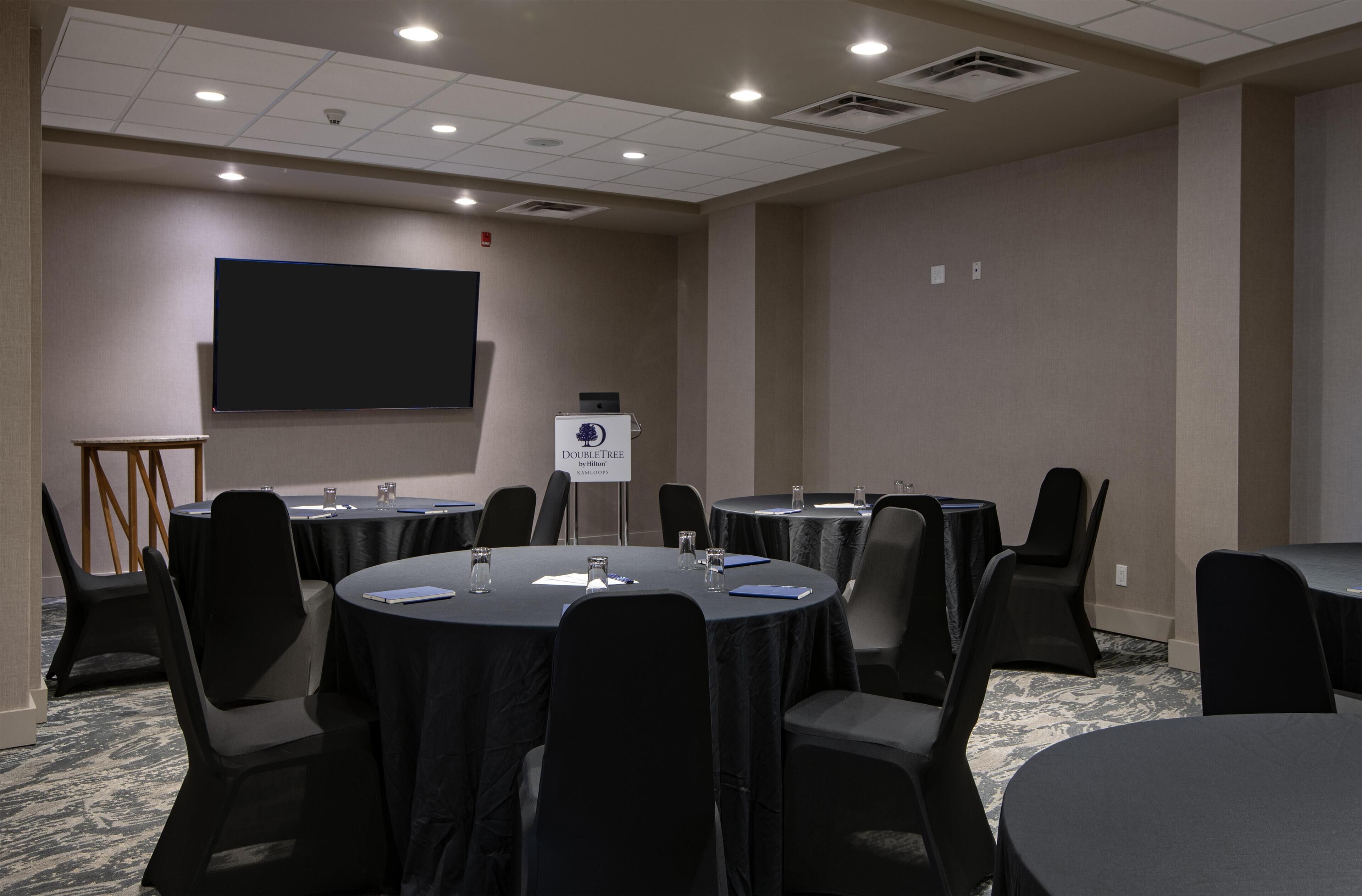A conference room with round tables, chairs, a projector screen, and a podium.