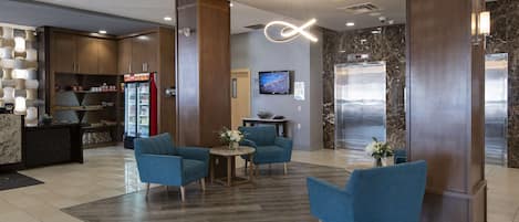 A lobby with a reception desk, seating area, vending machine, and elevator.