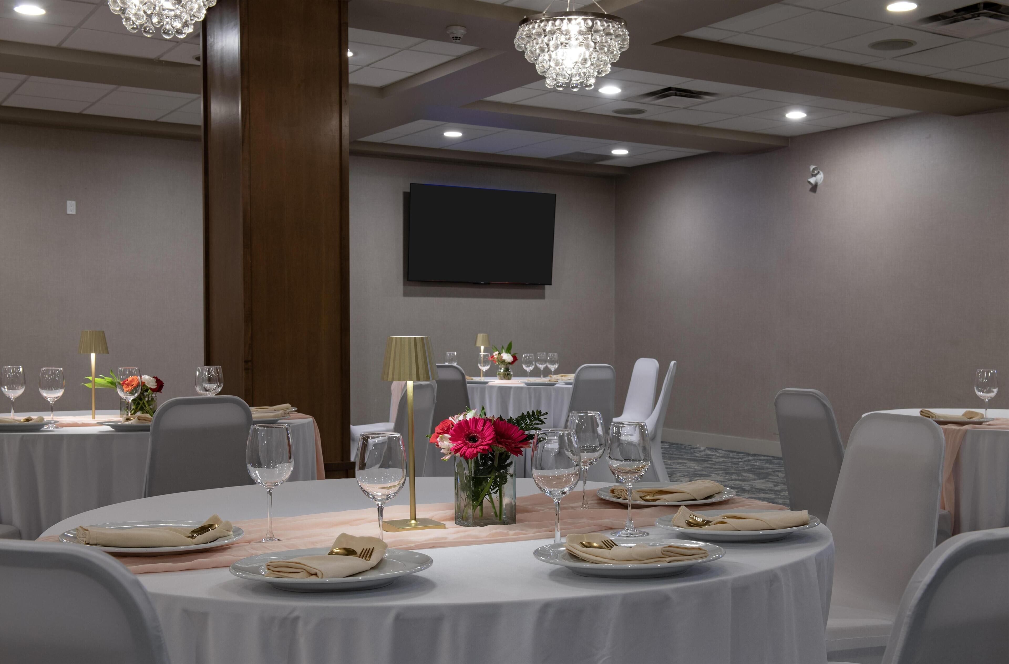 A conference room with round tables, chairs, a television screen, and a chandelier.