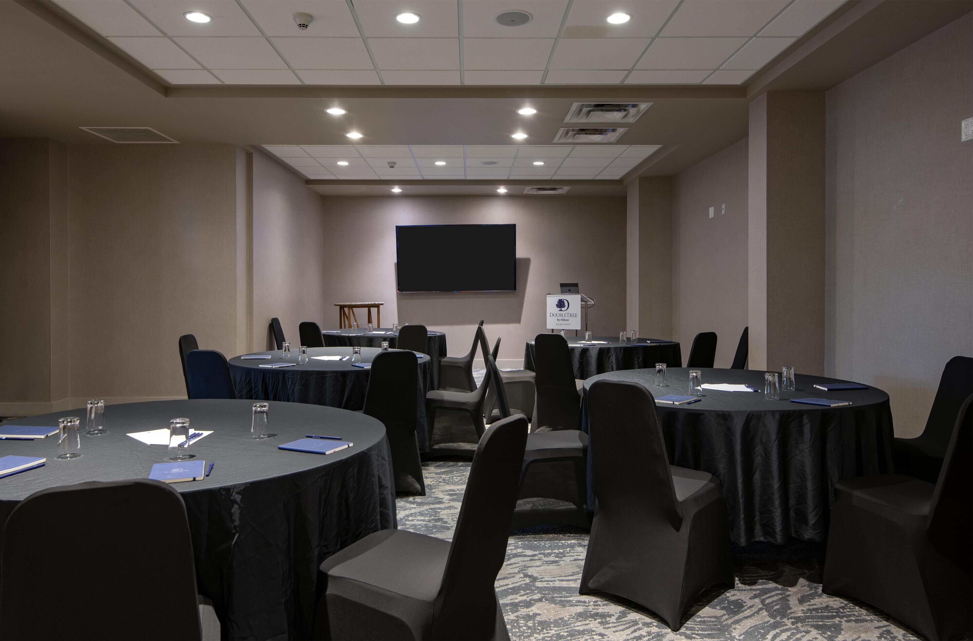 A conference room with multiple tables, chairs, a projector screen, and a podium.