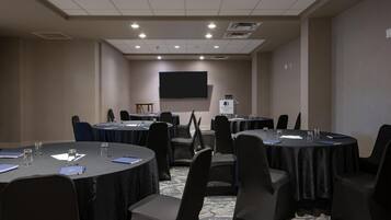 A conference room with multiple tables, chairs, a projector screen, and a podium.
