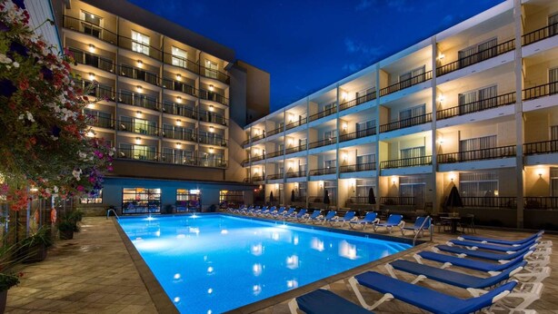 Un hotel con piscina, varios balcones y sillas de descanso.