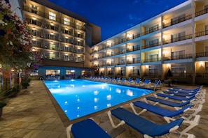 Un hotel con piscina, varios balcones y sillas de descanso.