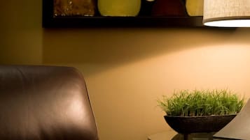 A leather chair, a round glass table with a bowl of green plants, and a wall-mounted abstract painting.