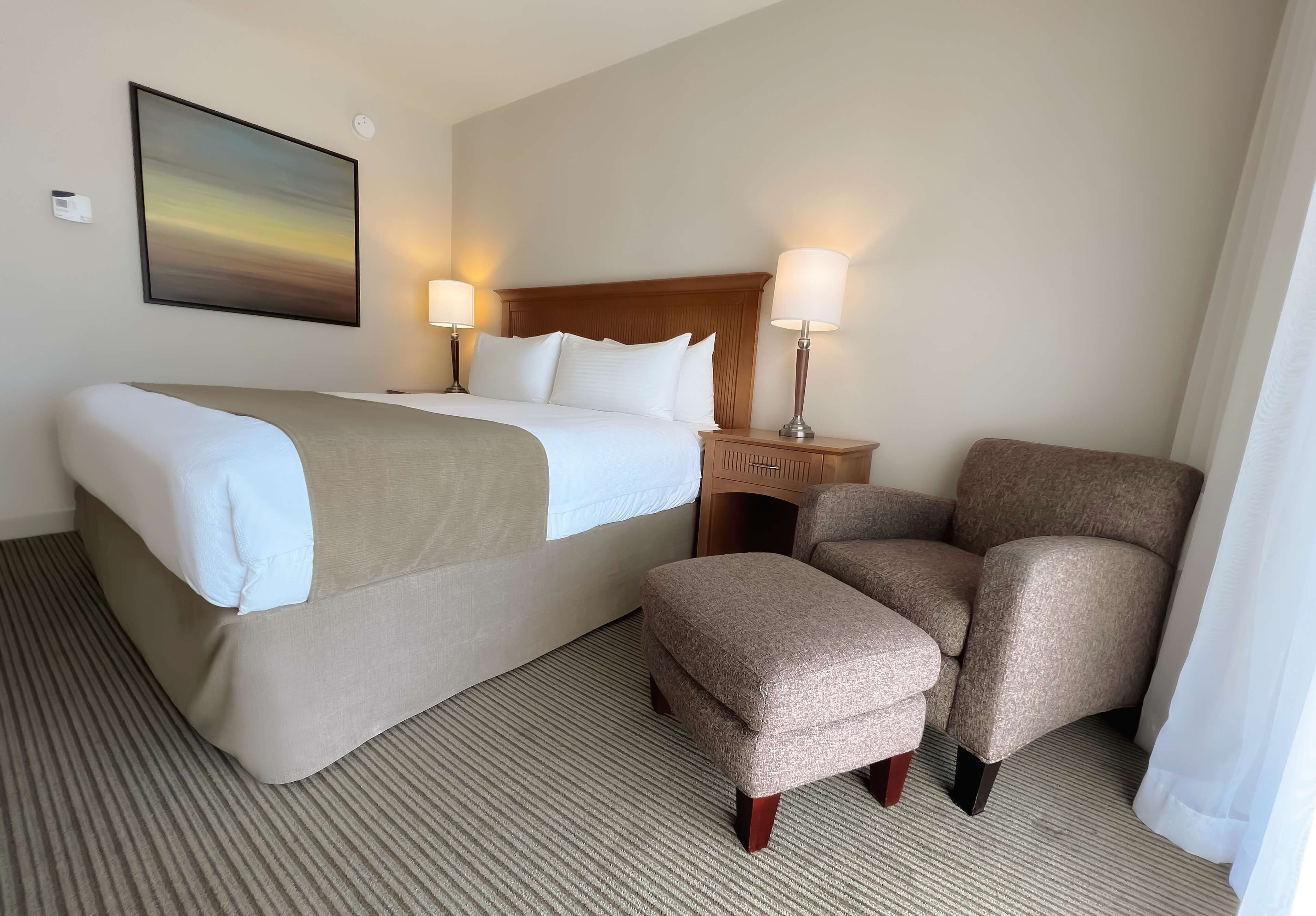 Een hotelkamer met een bed, twee fauteuils, een houten nachtkastje met lampen en een schilderij aan de muur.
