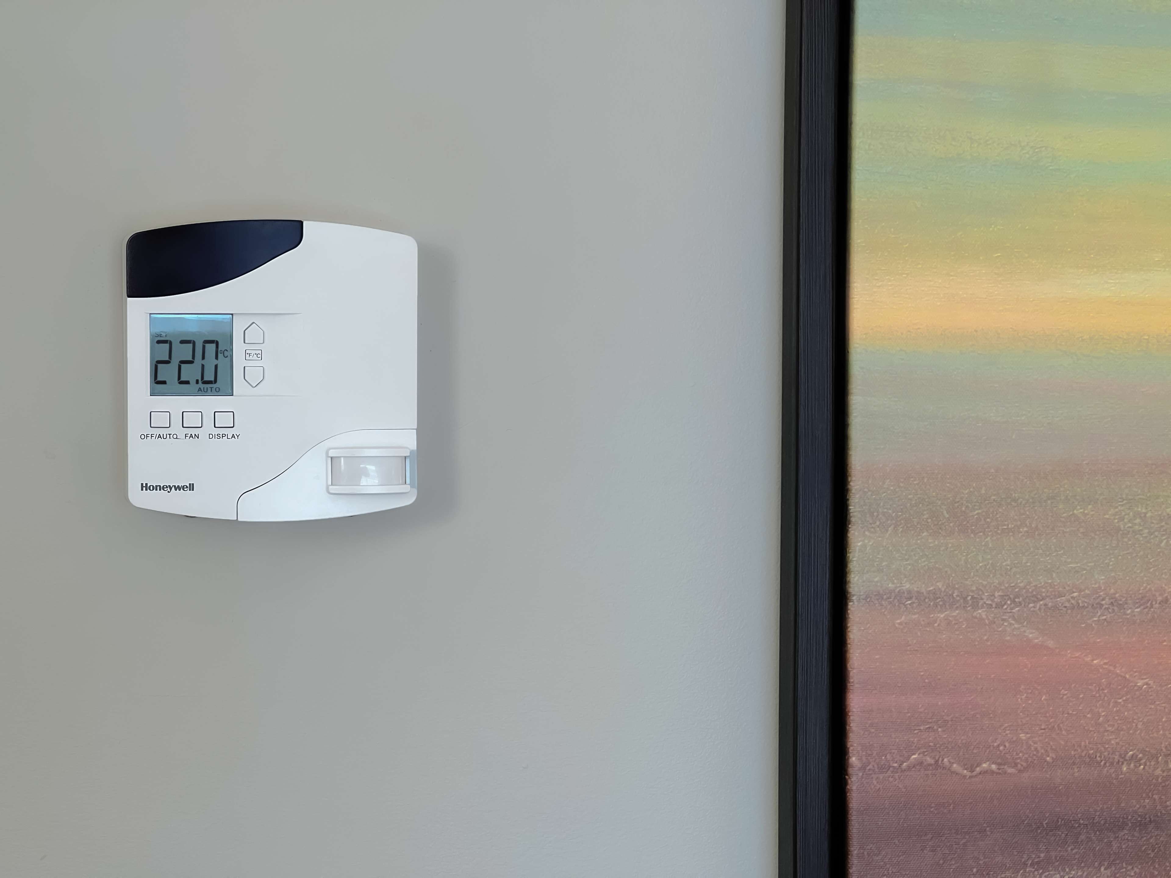 Un termostato Honeywell en una pared con pantalla digital que muestra 22.0°C.