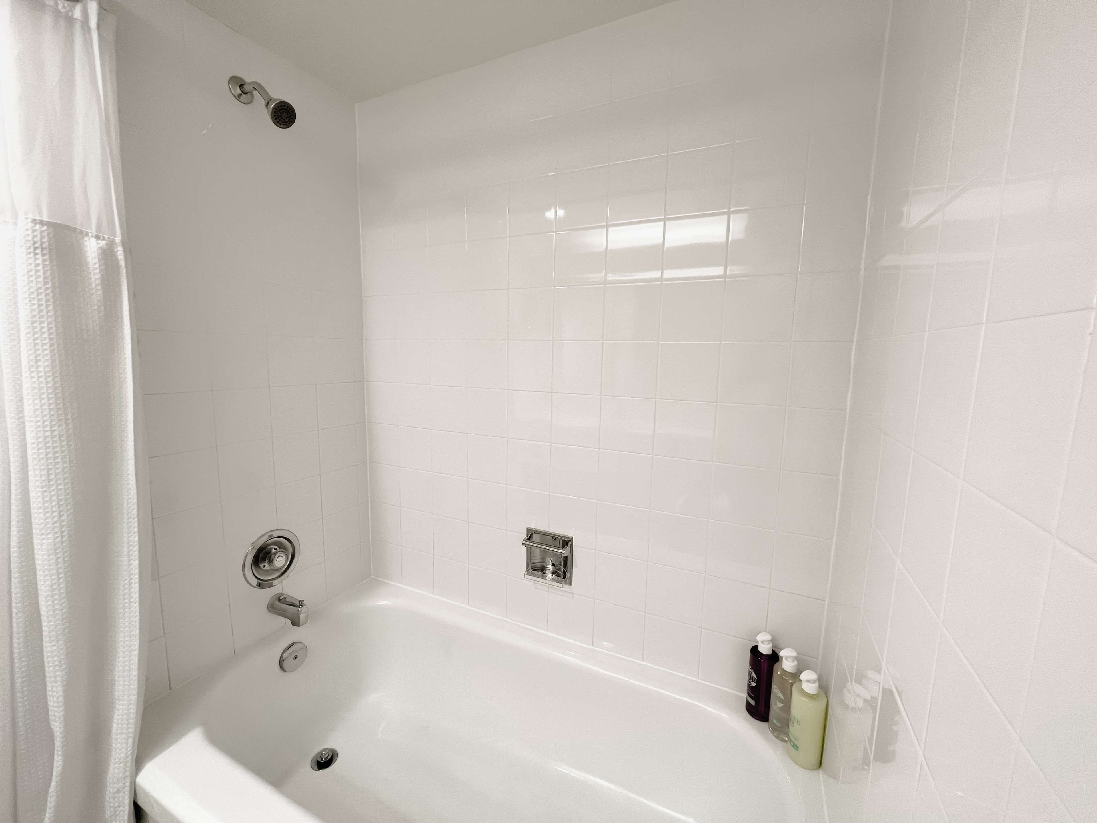 A white bathroom with a bathtub, a showerhead, and a hand dryer.