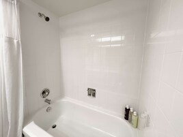 A white bathroom with a bathtub, a showerhead, and a hand dryer.