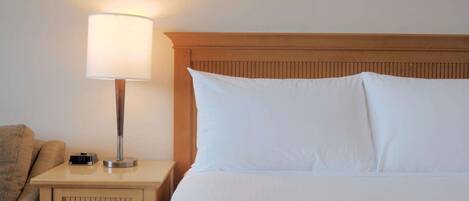 Una habitación de hotel con una cama, una mesita de noche con una lámpara y un reloj digital.