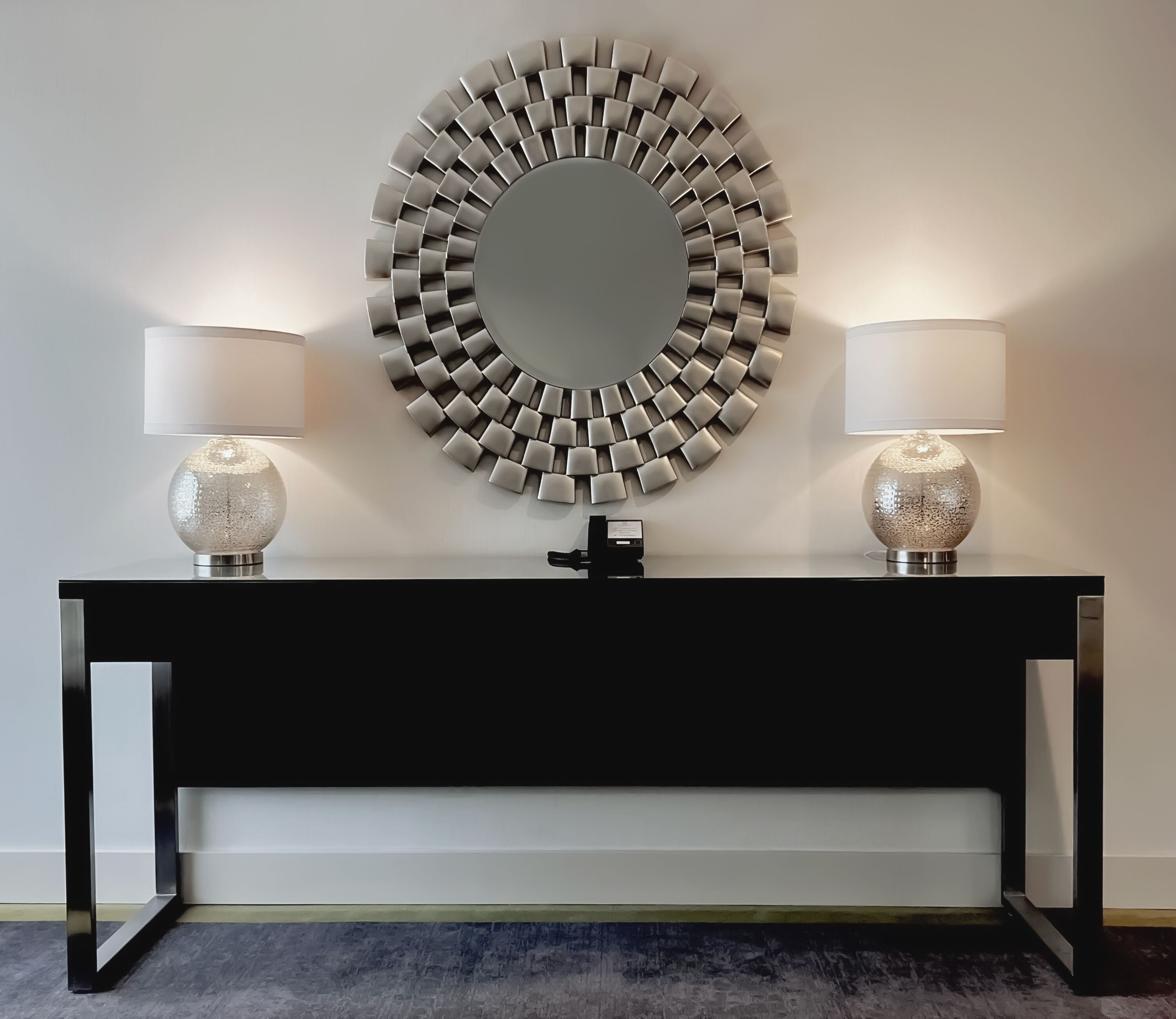 A black console table with two lamps and a decorative mirror.