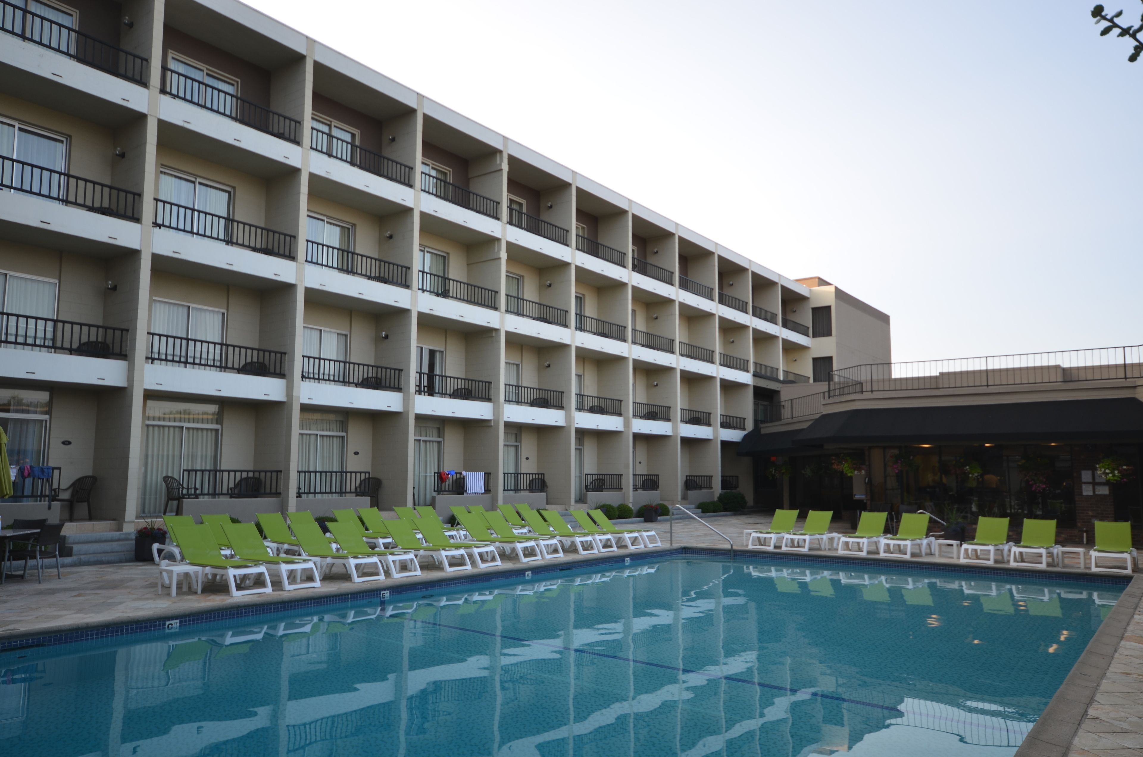 Un hotel con zona de piscina, varios balcones y sillones de jardín verdes.