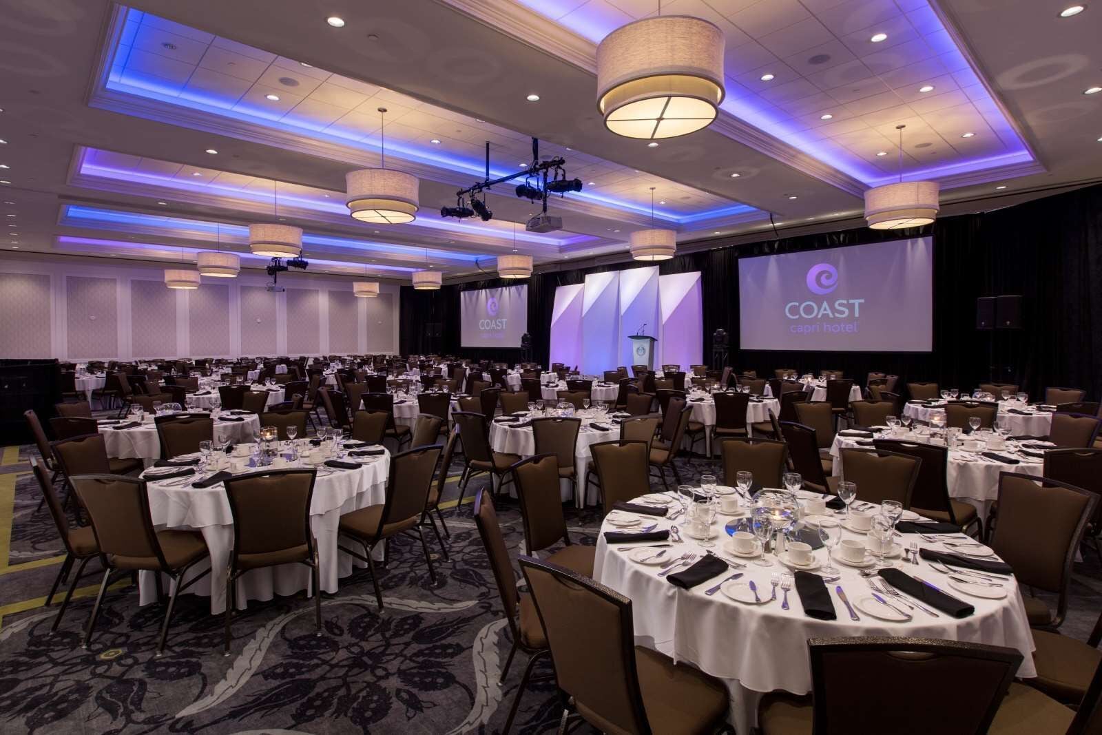 A conference room with multiple round tables, each set with white tablecloths, chairs, and dining essentials.